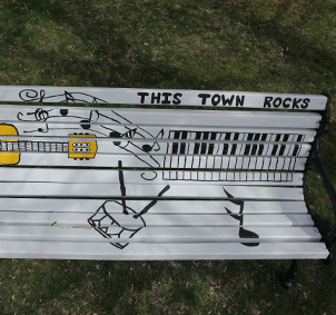Bemalte Parkbank mit Noten, Gitarre und Drums unter dem Titel This Town rocks